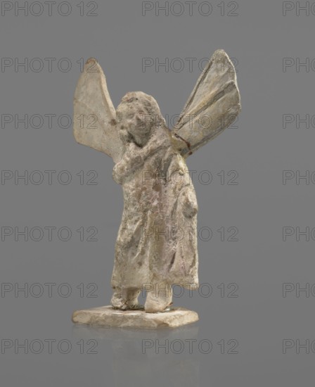 Terracotta figurine of Psyche, Young Psyche with butterfly wings, wrapped in a chlamys. Right hand rests on the chest, left hand rests along the body. Long hair falling on the shoulders is arranged in curls. Head turned to the left. Figurine placed on a rectangular base. 332–30 BC; Hellenistic period. Tanagra Greece. Figurine. Height 10.8 cm, width 7.5 cm, depth 3 cm., A small weathered figurine of a humanlike figure with large winglike extensions, standing on a flat base; the figure has a rough textured surface with worn features and a draped garment, and the wings are broad and slightly angled. The visible colors include pale off-white and beige with areas of light gray and muted brown, and faint traces of pale pink and yellow; the background is a uniform medium gray.