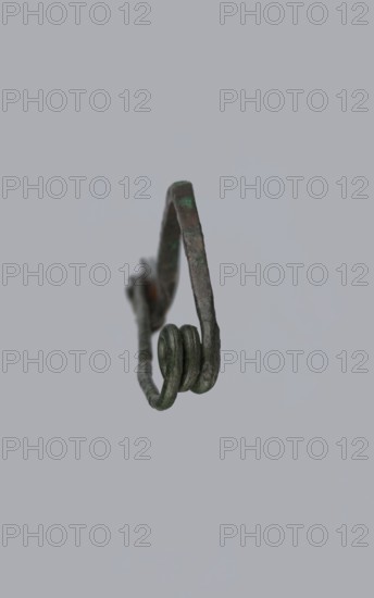 Arched fibula. Fibula with an arched bow; the pin emerges from a double-coiled spring. The sheath is in the form of a half-cylinder, cut to accommodate the pin. Material: bronze. Condition: good, greenish corrosion on the surface. Date: 7th–6th century BC 4th quarter of the 8th – mid-7th century BC, Raczynska. Place of origin: Italy . Jewelry, fibula. Creator: unknown., A close-up of a small metal object suspended against a plain pale gray background, showing a narrow curved frame with a looped end made of coiled metal; the metal surface appears aged with dark gray and greenish patina and some brownish spots, and the object has a textured, slightly irregular form with visible coils and bends.
