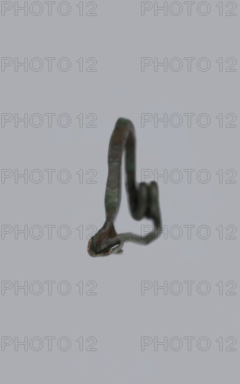 Arched fibula. Fibula with an arched bow; the pin emerges from a double-coiled spring. The sheath is a half-cylinder, cut to accommodate the pin. Material: bronze. Condition: good, greenish corrosion on the surface. Date: 7th–6th century BC 4th quarter of the 8th–mid-7th century BC, Raczynska. Place of origin: Italy . Jewelry, fibula. Creator: unknown., A close-up of a small twisted metal object suspended against a plain light gray background, showing a curved strip with a coiled loop and a pointed end; the metal appears weathered with greenish patina, dark brown and dark gray tones, and small hints of metallic bronze along some edges.