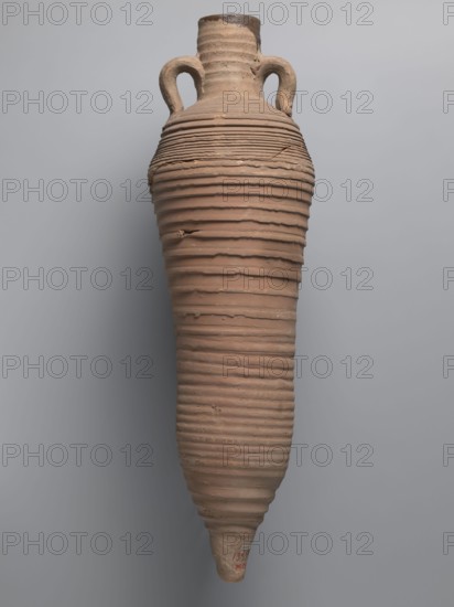 Amphora, unknown Egyptian workshop; amphorae, Egyptian amphoras, Egyptian ceramics, storage vessels, Coptic vessels, amphoras, amphoras, Nile clay, inscribed amphoras, inscribed vessels. Wine transport vessel with a strongly elongated belly, narrowed in the middle. Roller-shaped vices, approximately oval in cross-section, are glued to the central section of the neck with a straight rim. These connect to the upper section of the convex, steep shoulders. The base is conical and conically terminated. The entire surface of the vessel, brown and even, is covered with grooves of varying density and profile. The interior was impregnated with a black resinous substance, streaks of which are visible in the upper part of the neck. The clay is brown, alluvial Naqlun AC1A ceramic body type. On the upper part of the arms, between the vices, is an inscription in red paint: ICX. On the lower part of the arms, below the inscription, is a hollowed-out hole with a diameter of approximately 0.5 cm. 2nd h...