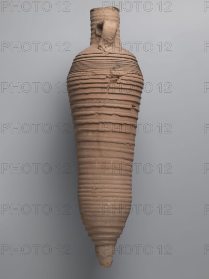 Amphora, unknown Egyptian workshop; amphorae, Egyptian amphoras, Egyptian ceramics, storage vessels, Coptic vessels, amphoras, amphoras; Nile clay; inscribed amphoras, inscribed vessels. Wine transport vessel with a strongly elongated belly, narrowed in the middle. Roller-shaped vices, approximately oval in cross-section, are glued to the central section of the neck with a straight rim. These connect to the upper section of the convex, steep shoulders. The base is conical and conically terminated. The entire surface of the vessel, brown and even, is covered with grooves of varying density and profile. The interior was impregnated with a black resinous substance, streaks of which are visible in the upper part of the neck. The clay is brown, alluvial Naqlun AC1A ceramic body type. On the upper part of the arms, between the vices, is an inscription in red paint: ICX. On the lower part of the arms, below the inscription, is a hollowed-out hole with a diameter of approximately 0.5 cm. 2nd h...