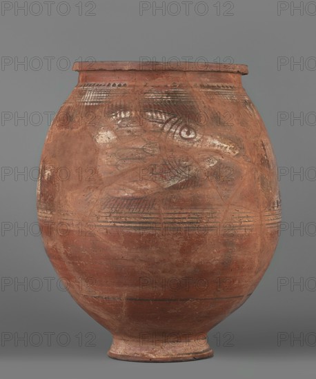 Pithos, unknown Egyptian workshop. Storage vessel with an ovoid belly, small annular high foot, and rim with a vertically beveled edge slightly protruding outward. At the point of greatest diameter there is an imprint of the rope used to tie the vessel during drying. Decoration only on the upper part of the belly: on both sides an image of a fish with a short body wider toward the tail—body and tail in side view, head viewed from above with visible eyes separated by a horizontal row of dots; fins rendered with lines. Fish bodies painted white with black contour and detail lines; each fish is flanked top and bottom by wide white lines with thin black lines painted on each. The fish are separated by a vertically painted braid on a white background, framed by black lines, with short diagonal lines terminating in dots. Painted Coptic storage vessel, figural, floral, and impressed decorative elements. 6th–7th century, Edfu. Vessel; height 43.8 cm, width 34.1 cm., A large rounded pottery ves...