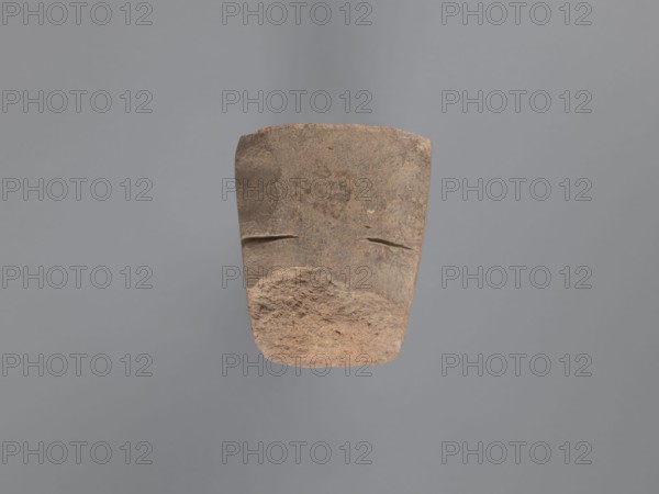 Pyramidal clay seal with a roughly square stamp surface and rounded corners. Shallow incisions at mid-height. Base engraved with a letter-like motif—either a geometric B or an M resting on the base—beside a small round recess. Upper part is impressed; chippings on the base. Visible kaolin clay, pink-beige. 6th–7th century, unknown South Egyptian workshop; Edfu. Seal/stamp. Height 6.1 cm, width 5.5 cm. Geometric decorations, monograms, engraved decorations, stamp impressions., A roughly rectangular stone object with a worn, textured surface suspended against a plain gray background; the stone shows earthy tones of brown, tan, and reddish-brown with rough, pitted areas and smoother, flatter areas; there are two shallow horizontal grooves near the upper middle and a more eroded, uneven lower portion with granular texture; overall the lighting highlights the stone’s surface irregularities and subtle color variations.