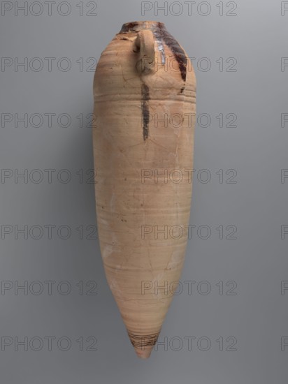 Amphora, unknown Gazan workshop Gaza Strip — Large LRA 4 amphora of a spindle-shaped form, almost cylindrical in the central part. Hemispherical shoulders; conical, flat-topped lower part. Rim weakly accentuated, rounded, with slightly thickened edge. Two loop handles placed in the upper part, reinforced below with added clay. Ceramic fabric likely contains limestone inclusions visible on the surface. Outer surface beige-orange, upper part covered with slipped/soaked clay to produce a rough finish. Ribs visible in upper and lower parts; deep grooves in the lower portion. Interior coated with black resin impregnation, some resin leaked onto the shoulder. Near one handle a small, barely visible Coptic inscription in black ink; a large inscription in red paint runs along the vessel, though no inscriptions were recorded on the amphora. Probably 4th quarter of the 6th–7th century. Findplace: Edfu. Function: transport/storage amphora. Dimensions: height 75.3 cm; rim diameter 10.0 cm; body di...