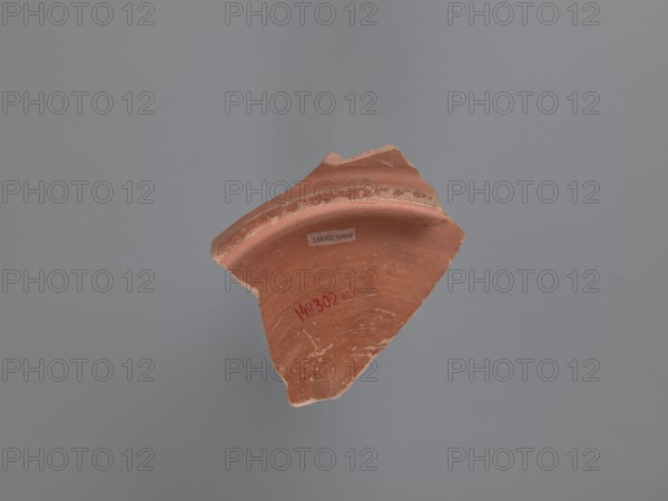 Plate fragment, unknown Aswan workshop, plates, tableware, Aswan pottery, Egyptian pottery, Egyptian sigillata, Coptic vessels, Coptic pottery, impressed decorations, stamped decorations, stamps, kaolin clay. Fragment of the bottom of a plate with a ring-shaped foot. Pink kaolin ceramic mass Gempeler 1A. The surfaces are polished and covered with a reddish-brown engobe. The vessel is decorated internally, on the bottom of the bowl, using pressing and engraving techniques. These create a composition whose central element is a rosette impressed with almond-shaped stamps forming a pattern. It is surrounded by five concentrically engraved grooves. The band surrounding them consists of a double-course zigzag, made with an impressed roulette. The fields between the zigzag arms are filled with rhomboidal impressions of a stylus . The entire composition is enclosed by eight concentrically engraved grooves. 5th–6th century, vessel, plate, height 2.7 cm, width 11.4 cm, diameter 10 cm bottom, A b...