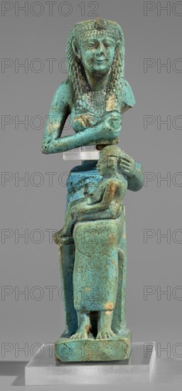 Figurine of the goddess Isis nursing Horus, Harpocrates myth., Isis myth.; Egyptian deities, female figurines; Egyptian art, 664–332 BC, Late Period, Egypt; figurine, A small turquoise-colored figurine of a seated adult with braided hair and a headdress holding a smaller seated child on their lap, both rendered in a weathered bluish-green material with areas of darker green and brownish discoloration, placed on a clear rectangular base against a neutral gray background.