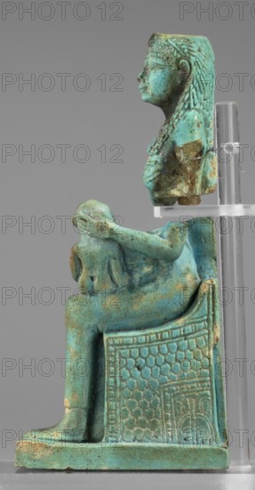Figurine of the goddess Isis nursing Horus; Harpocrates myth., Isis myth.; Egyptian deities; female figurines; Egyptian art; 664–332 BC, Late Period, Egypt; figurine;, A small turquoise-green glazed figurine showing a seated female figure in profile on an ornate chair, with long braided hair, a visible arm extended forward holding a rounded object, and detailed texture on the chair back and sides; the glaze shows areas of darker green and brownish-green spotting and wear, and the composition is supported by a clear stand against a plain gray background.