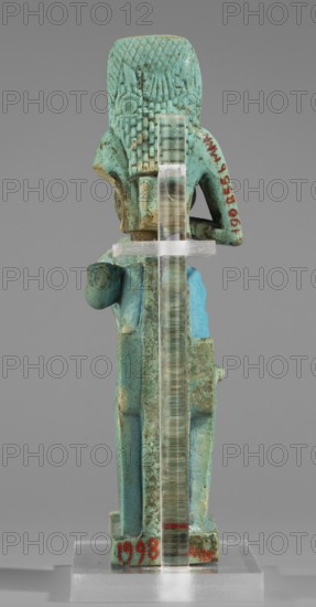 Figurine of the goddess Isis nursing Horus; Harpocrates myth., Isis myth.; Egyptian deities; female figurines; Egyptian art; 664–332 BC, Late Period, Egypt; figurine;, A small turquoise-blue and greenish figurine shown from the back, standing on a rectangular base, with a clear vertical support running down its center; the figure has a textured headpiece or hair pattern, a curved arm outline visible on one side, areas of darker green and brown weathering or patina across the surface, and a neutral gray background.