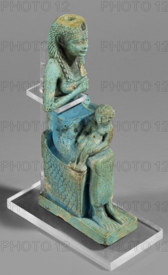 Figurine of the goddess Isis nursing Horus, Harpocrates myth., Isis myth., Egyptian deities, female figurines, Egyptian art, 664–332 BC; Late Period, Egypt, figurine, A small turquoise and green glazed statuette of a seated female figure on a rectangular base, shown in profile, wearing a detailed headdress and a long patterned garment; she holds a small child on her lap, both figures rendered in the same turquoise-green tones with areas of darker green and pale beige weathering, and the sculpture sits on a clear acrylic support against a neutral grey background.