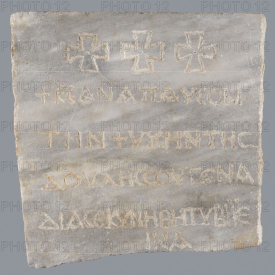 Epitaph of Gennadii;, Inscription: Greek; epitaph in five lines, rounded letters 1.5–2.0 cm high, average line spacing 2.5 cm. Material: fine-crystalline blue-gray marble. Date: 6th–7th century. Place of origin: Constantinople, Byzantine Empire 476–1453. Description: lower edge of slab chipped; preserved part cracked transversely halfway up. Upper part above inscription bears three symmetrically arranged Maltese crosses. Dimensions: height 29.5 cm, width 29.5 cm, depth 2.0 cm., A rectangular slab of pale stone with a rough edge, showing a group of shallow carved crosses near the top and several rows of incised markings across the surface; the stone has a marbled texture with streaks and patches of light gray and off-white, with areas of beige and faint brown discoloration, and the carvings appear filled with a slightly darker beige residue.