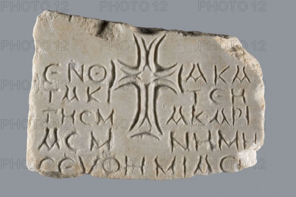 Euphemia's Epitaph, unknown author, Greek inscriptions, tombstone inscription. Preserved central fragment of a white marble slab. Top and bottom are chipped, but the inscription is intact. In the center of the slab is a large cross with almost equal arms widening at the ends. The inscription is placed between the arms of the cross. Rounded letters are placed between marked thin lines; letter height 1.5–2.1 cm, average line spacing 0.2 cm. The inscription comes from Bithynia or Constantinople. 6th–7th century, Asia Minor. Greek inscription, epitaph stele; height 15.0 cm, width 20.5 cm, depth 3.2 cm., A roughly rectangular pale beige stone slab with an irregular top edge and worn corners, featuring carved shallow grooves and a prominent symmetrical raised cross-like motif in the center with flaring curved arms; the surface shows weathered texture and slight discoloration with areas of darker beige and pale gray, and there are several rows of incised marks arranged around the central moti...