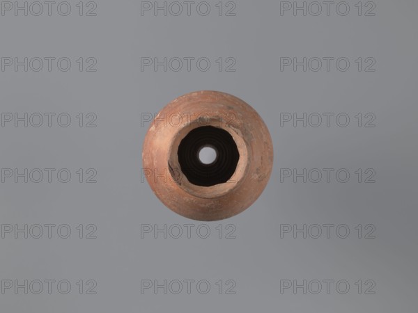 Bottle, Egyptian workshop, painted Coptic pottery, painted pottery, geometric decorations. Low, wide, annular foot; belly walls widely flared at the bottom, bent inward at approximately one-third of the vessel; neck reflected. Decoration painted in black and white, banded. Below the neck, a zigzag band painted in white, adorned with a diagonal black check motif; below, a strip of vertical lines painted alternately with black and white paint, framed at top and bottom by double black stripes. LRO type item. Nile clay, low porosity, with distinct golden mica flakes. 6th century, Egypt; vessel. Height 17.5 cm, width 11 cm body, diameter 8 cm outer rim., A round, weathered clay pot viewed from above with a rough, uneven rim and a dark hollow center, sitting against a smooth gray background; visible colors include terracotta orange and brown on the pot, dark brown and black in the interior, and various shades of gray in the background.