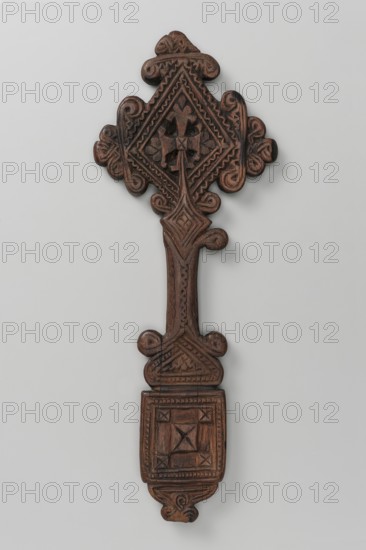 Hand cross. The arms of the cross are rhombus-shaped, the tops decorated with volutes topped with trefoils. The handle, decorated at the top and bottom with volutes, transforms into a rhombus at the top and into a triangle with rounded tops at the bottom, which then becomes a rectangular plaque topped with a smaller triangle topped with a trefoil inset. Decoration on both sides, with four small circular openwork cutouts in the central part of the arms. Side A: In the center of the rhombus is a motif of an isosceles cross whose arms are topped with volutes and trefoil finials. The rhombus connecting the arms of the cross with the handle is decorated with a quatrefoil motif. The handle has a vertical zigzag stripe. The triangle is filled with a geometric ornament enclosed in a rope-like frame. The plaque is decorated with a central square motif with marked diagonals, whose vertices are adjoined by four smaller squares, also with marked diagonals. The triangle under the plaque and the ins...