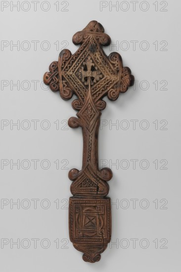 Hand cross, Ethiopian workshop. The arms of the cross are rhombus-shaped, the tops decorated with volutes topped with trefoils. The handle, decorated at the top and bottom with volutes, transforms into a rhombus at the top and into a triangle with rounded tops at the bottom, becoming a rectangular plaque topped with a smaller triangle topped with a trefoil inset. Decoration on both sides, with four small circular openwork cutouts in the central part of the arms. Side A: In the center of the rhombus is a motif of an isosceles cross whose arms are topped with volutes and trefoil finials. The rhombus connecting the arms and handle is decorated with a quatrefoil motif. The handle has a vertical zigzag stripe. The triangle is filled with a geometric ornament enclosed in a rope-like frame. The plaque has a central square motif with marked diagonals, whose vertices are adjoined by four smaller squares, also with marked diagonals. The triangle under the plaque and the inset are decorated with ...