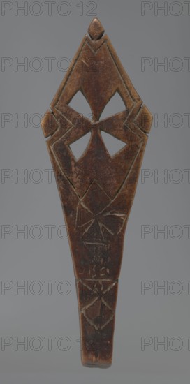 Hand cross fragment, Simple engraved decoration on the surface with four triangular cutouts arranged in the form of a cross. Below the holes are two rather carelessly engraved crosses; the reverse is also decorated with a cross motif. Decoration engraved with a thin, shallow line. Dark wood. 20th century, Ethiopia. Cross; height 26 cm, width 8 cm., A carved wooden object with a tapered elongated shape and a pointed top, showing a dark brown surface with lighter worn areas and scratches; the upper section has symmetrical cutout shapes forming a geometric pattern and raised carved edges, and the lower section features incised triangular and star-like designs; the background is a uniform muted gray.