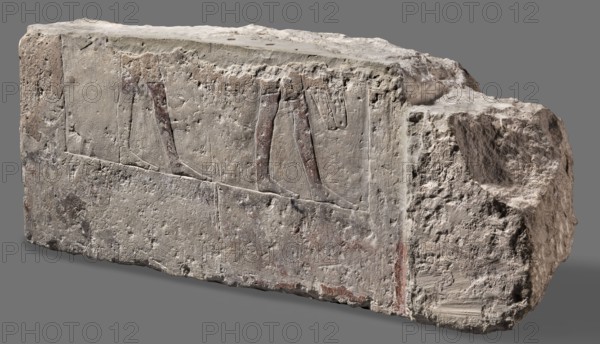 Fragments of wall decoration from the mastaba of the dignitary Tepemankh, Niuserre ruler of Egypt; ca. 2445–2421 BC, Tepemankh ca. 2445–2421 BC, revindication provenance, sacrificial artists, scribes, mastabas, shipwright iconography, Egyptian architecture, sepulchral funerary architecture, scenes of boat building and bringing funerary offerings, c. 2445–c. 2421 BC; Old Kingdom, 5th Dynasty Nyuserre's reign, Abusir, bas-relief; height 26 cm, width 302 cm, depth 16 cm, weight 140 kg, A weathered rectangular stone block with rough, eroded surfaces sits against a neutral gray background, showing faint carved reliefs of a group of legs and feet on one face. The stone's surface displays a range of colors including pale beige, light gray, off-white, dusty brown, and traces of muted reddish-brown within the carved areas and along some edges. The top surface is lighter and smoother with some irregularities, while the front face has textured pitting and shallow incised lines forming the leg sha...
