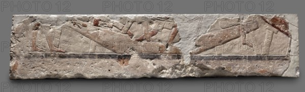 Fragments of wall decoration from the mastaba of the dignitary Tepemankh. Scenes of boat building and bringing funerary offerings. Old Kingdom, 5th Dynasty, reign of Niuserre c. 2445–2421 BC. Abusir. Bas-relief; height 26 cm, width 302 cm, depth 16 cm, weight 140 kg. Includes depictions of sacrificial artists, scribes, shipwright; funerary/sepulchral architecture; inscriptions naming Niuserre and Tepemankh., A rectangular stone relief with worn carved figures and a rough textured surface, showing a horizontal composition of reclining and standing human-like forms rendered in shallow incisions and low relief; the stone displays areas of smooth carving and pitted erosion, with visible remnants of painted areas in shades of red and brown, and traces of darker gray and black along a horizontal band; the overall stone color is off-white to beige with spots of darker discoloration and weathering, and the background behind the relief is a uniform medium gray.