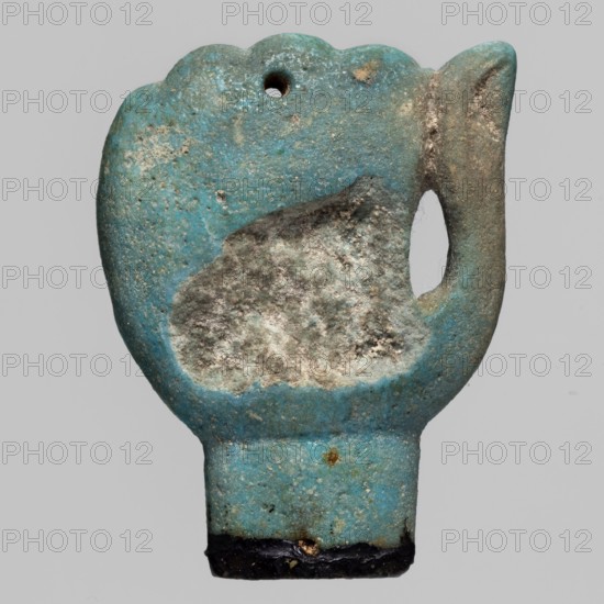 Amulet - left fist element of a mummy net, mummification equipment amulet in the form of a left fist, Late Period, Egypt, 664–332 BC; mummy net component; height 4.9 cm, width 3.6 cm., An irregularly shaped object resembling a pendant or amulet with a rounded top and a narrow rectangular base, shown against a plain light gray background, with a small rounded hole near the top and a teardrop-shaped cutout near one side; the surface shows a worn, textured appearance with a central patch of rough, lighter, almost white-gray material surrounded by a turquoise-blue field that varies in intensity, along with areas of darker blue-green, pale beige, and spots of brownish discoloration, and a narrow strip of dark, almost black material along the bottom edge.