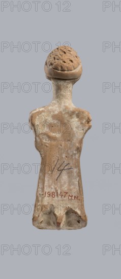 Terracotta figurine of a woman, terracotta, female molded figurine, Greece, orange clay, surface covered with whitewash. Woman dressed in a short, pleated chiton girdled at the waist. Long, thick neck and disproportionately small head with an oval face. Hair combed upwards and tied in a bun, held in place by a headband tenia tied in a bow at the top of the head. The back of the figurine is unfinished. The figurine originally had separately attached arms and legs below the knees, as evidenced by a recess and perforations for hooks. Condition: missing arms and legs, whitewash worn away. c. 400 BC, Greece, toy. Height 10.1 cm, width 3.5 cm., An upright worn figurine with a rounded textured head and a narrow neck leading to sloping shoulders and an elongated torso, displaying a weathered surface with patches of lighter and darker areas; the object shows rough, chipped edges and small pits, and the visible colors include shades of tan, brown, beige, and off-white against a plain gray backgr...