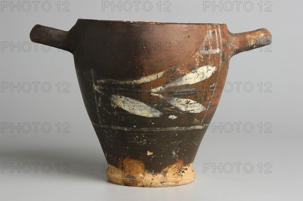Black-finished skyphos with painted decoration on the finis, white decoration: A = B - laurel branch, IV waC, Etruria, vessel, height 9.7 cm, width 9.2 cm, A ceramic vessel with a wide rim that narrows to a small base, shown from the side with a handle extending from each side; the vessel surface shows worn paint and decorative markings in a lighter color against a darker background, with visible areas of chipped and aged texture; the colors visible include brown, dark brown or black, off-white or cream, and hints of tan and orange on the worn base and rim; the background is a neutral light gray.