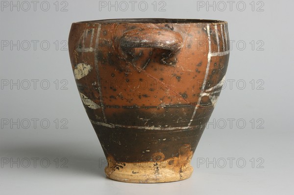Black-finished skyphos with painted decoration on the finis, white decoration: A = B - laurel branch, IV waC, Etruria, vessel, height 9.7 cm, width 9.2 cm, A conical ceramic vessel with a rounded rim and a small protruding handle on its upper side sits against a plain light gray background, showing an overall reddish-brown body with darker brown bands and mottling, patches of lighter beige near the base, and traces of pale white painted markings; the surface appears worn with scratches, spots of darker discoloration, and areas where the finish has chipped away, revealing rougher beige material at the foot.