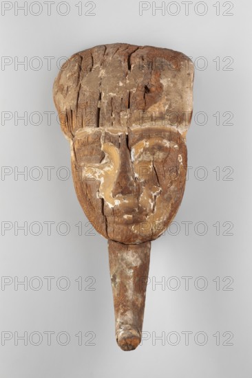 Sarcophagus mask. Sarcophagus mask with a preserved face, the middle part of a wig, and a false beard. The eye modelling emphasizes the convexity of the upper eyelids and eyebrow arches. The nose is small with a slight hump. The lips are full with a carefully crafted hollow where the lips meet. The cheeks are modeled quite flat. The wig, pulled over the forehead, reaches almost to the eyebrows. A false beard with a curved end adheres to the chin. Face height: 13 cm. The polychrome is preserved only fragmentarily: slightly larger fragments of yellow paint with the plaster base survive around the mouth; in the inner corners of the eyes and on the side of the face; traces of blue remain on the chin. The back of the mask is flat, with three holes containing fragments of pegs. Date: 16th–7th century BC; New Kingdom–Third Intermediate Period. Place of origin: Thebes, Egypt. Type: sarcophagus mask. Dimensions: height 35.5 cm, width 16.5 cm, depth 10.5 cm. Weight: 0.874 kg., A carved wooden fa...
