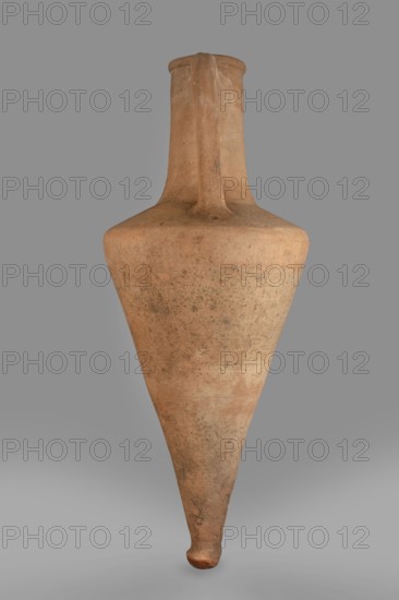 Transport amphora, slightly sloping shoulders. High and narrow neck, narrowing at the top and ending in a spout. Thick, ribbon-shaped handles, divided by a groove. In the center - a recess pressed with a finger in wet clay. 1st half of the 4th century BC, Thasos. Vessel, transport amphora, height 66 cm, diameter 23 cm., A tall, narrow ceramic vessel with a long tapered body and a pointed base, displaying a handle that runs from the neck down toward the shoulder; the surface shows a weathered, slightly rough texture with mottled patches. The visible colors include shades of tan, light brown, beige, and hints of darker brown spots, set against a neutral gray background.