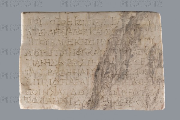 Titulus of the tomb of the Systilians; creator, tombstone inscription in Greek; 2nd–3rd century; Phrygia; Greek inscription; tombstone; height 26.0 cm, width 38.0 cm, depth 4.5 cm, A rectangular stone slab with a smooth, light surface showing a group of shallow incised markings arranged in horizontal rows, with the right side exhibiting a darker, marbled discoloration and subtle stains; the slab edges are slightly worn and uneven, and the overall colors visible are off-white, beige, pale gray, and darker gray-brown marbling.