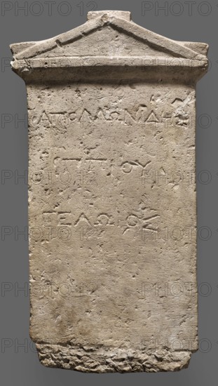 Tombstone of Apollonides with Greek inscription. Rectangular slab with three lines of Greek inscription, topped with a triangular tympanum. Tombstone of Apollonides, son of Hippias of Gela, 300–250 BC; Ptolemaic period. Found at Zawiyet el-Mayetin near Minia, Kom el Ahmar. Greek inscription. Height 58.5 cm, width 32 cm, depth 9 cm, weight 25.5 kg., A tall rectangular stone slab with a triangular pediment at the top, showing a rough, weathered surface and chisel marks; the stone is mostly beige and light tan with areas of darker brown discoloration and small patches of off-white; the top edge has a raised triangular molding and some chipped and uneven edges, the sides are straight but worn, and the bottom edge is irregular and broken with a jagged texture; the face of the slab has shallow, incised grooves and a few shallow depressions and scratches across its surface, giving it a pitted appearance; overall the slab appears solid and aged with a muted palette of beige, tan, brown, and of...