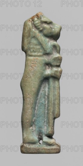 Amulet of Hapi. Relief figurine of Hapi — one of the Sons of Horus. Hapi shown in right profile with a mummy-like body and a baboon's head covered with a wig, holding a folded cloth in front of him. Smooth back with two holes for attaching the figurine. Part of a set of four Sons of Horus. Date: 664–30 BC Late Period–Ptolemaic Period, Egypt. Amulet; height 4.6 cm, width 1.4 cm., A small vertical figurine of a standing anthropoid figure with a stylized head and mane-like detail, rendered in a weathered bluish-green faience with areas of brownish discoloration and pale grayish spots; the figure stands on a rectangular base, with a draped element along one side and rounded limb forms, and surface pitting and worn edges visible across the object.