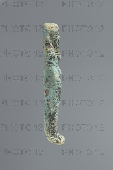 Ushabti, mummy-shaped figurine. Flat back. Arms crossed on the chest, only the hands protruding from under the shroud. Hoes in both hands. Tripartite wig on the head. Facial details illegible. Not inscribed. 664–332 BC, Late Period, Memphis, Egypt. Ushabti; height 8.5 cm., A narrow vertical carved figure with a rounded head and elongated body, showing a few areas of rough texture and pitting, suspended against a plain gray background; the surface displays mainly greenish-blue and turquoise tones with patches of darker brown and black corrosion and a few lighter beige spots, and the lower end curves slightly outward.