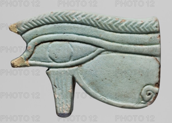 Amulet — udjat eye; protective amulet, grave good. Amulet in the shape of an udjat eye with very carefully carved details; the eyebrow is carved in a herringbone pattern. A hole for a thread runs across it. The amulet is in the form of a very thick plate with light blue glaze. Materials/measurements: amulet, height 3 cm, width 4.5 cm, depth 0.9 cm. Date/place: 664–525 BC, Late Period, 26th Dynasty, Berytos. Maker: unknown., A pale blue-green carved object shaped like a stylized eye with raised curved lines and a rounded central area, showing areas of worn beige and brown along the edges and small darker speckles across the surface, with a textured zigzag band along the top, a protruding tab at the bottom, and a small spiral motif near one corner.