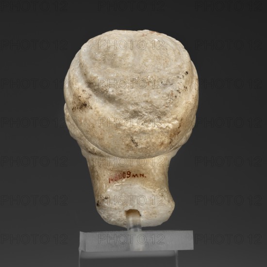 Head of a woman in a bonnet; Greek sculpture of a female portrait showing hairstyle details; 5th century BC, Greece;, A close-up of a small sculpted object photographed from the back, showing a rounded top with textured, uneven surface and worn edges in creamy white with areas of beige, light brown, and darker brown spots; the lower section narrows and shows a smoother, slightly polished surface in similar creamy white and beige tones, with a small rectangular hole near the bottom through which a translucent rod passes; the object rests on a rectangular clear base against a dark gray background.