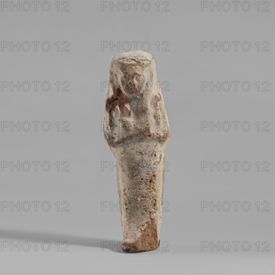 Ushabti. Mummy-shaped figurine made of clay, painted cream with black details. Arms crossed on the chest, right hand folded over left; both hands hold hoes rendered in relief and painted black. Wears a smooth, tripartite wig; facial details marked in black. Back is smooth. No inscription. c. 1069–c. 945 BC; Third Intermediate Period, 21st Dynasty, from Edfu . Ushabti; height 6.3 cm, width 2 cm., A small weathered figurine stands upright against a plain light gray background, showing a rounded head and an elongated tapering body with indistinct facial and limb features; the surface appears rough and pitted with areas of flaking and erosion, and the visible colors include off-white, beige, light brown, and darker rust-brown patches.
