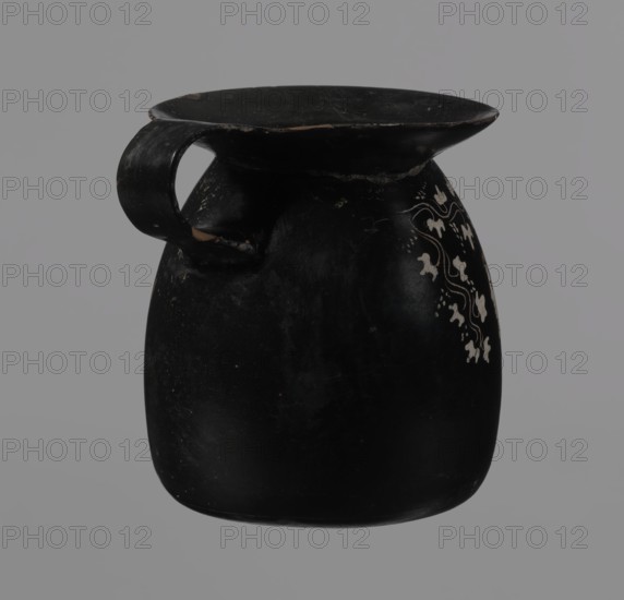 Gnathia-style mug, antique vessel, mug; Gnathia style Southern Italy, Apulia; 4th–3rd century BC. Red clay with glossy varnish, white-painted decoration and yellow retouching. Flat bottom, convex belly tapering at the top into a wide spout; band-like lip. Decoration mainly opposite the lip on the upper belly: three elongated female heads turned left, shown in profile with large eyes and hairstyles shaded with yellow, surrounded by an ornament of ivy fruit and leaves. Vessel/cup., A dark rounded ceramic vessel with a wide flat rim and a single curved handle is shown against a gray background; the vessel is primarily black with a slightly worn surface and small areas of lighter wear, and one side features a decorative pattern of pale, cream-colored floral shapes and flowing lines.