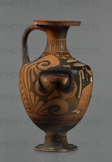 Red-figure hydria, Southern Italy Apulia. Hydria vessel, 330–320 BC. Black glossy engobe, some elements painted white. Red-figure hydria on a high, profiled foot with slightly sloping shoulders; narrow neck widening toward a wide, flat rim rolled outward and decorated with vertical-line ornamentation. Three handles: two vertical below the shoulders and one horizontal from the rim to the shoulders; palmettes next to the handles. Frontal belly scene: a woman seated on a rock, wearing a long chiton; in her right hand she holds two flowers, in her left a kalathos and a wreath. Behind her a plate lies on the ground, and in front of her a rolled-up cloth hangs., The image shows a single ceramic vessel with a rounded body, a narrow neck that flares into a flat rim, a single curved handle, and a small pedestal foot. The surface features painted decorative motifs including spirals, curving leaflike forms, and bands of patterns. Visible colors include terracotta orange, black, dark brown, and li...