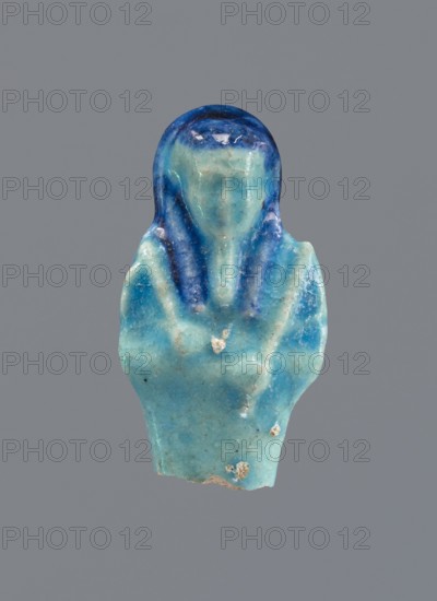 Shabti, Mummy-shaped figurine, funerary gift, back supported by a pillar/pilaster. Legs missing. Arms crossed on the chest, right folded over the left. In the right hand, a hoe; in the left, a pickaxe. On the back, a bag slung by a single string over the left shoulder. On the head, a three-part smooth wig painted navy blue. Long braided beard. Not inscribed. 664–332 BC, Late Period, Egypt. Height 5.1 cm., A small carved object shaped like a simplified human figure with a rounded head and draped shoulders, showing a smooth surface with visible wear and small chips; the piece displays shades of blue and turquoise with darker blue accents around the head and vertical darker streaks along the shoulders, and a neutral grey background.