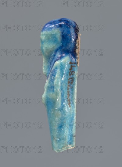 Shabti, mummy-shaped figurine, funerary offering. Mummy-shaped figurine supported at the back on a pillar. Legs missing from the knees down. Arms crossed on the chest, right folded over left. In the right hand is a mattock, in the left an axe. On the back is a bag slung on a string over the left shoulder. Convex tools. On the head is a smooth, tripartite wig and a long, straight beard. Not inscribed. 664–332 BC, Late Period, Egypt. Shabti; height 6 cm., A small sculpted figure rendered in shades of blue and turquoise with a glossy surface, shown in profile against a plain gray background; the figure has a rounded head with darker blue on top and lighter turquoise on the face and body, a suggestion of a draped garment with smoother darker blue along the shoulders, and a narrow elongated lower portion with areas of mottled lighter and darker blue and some pale, slightly rough edges.