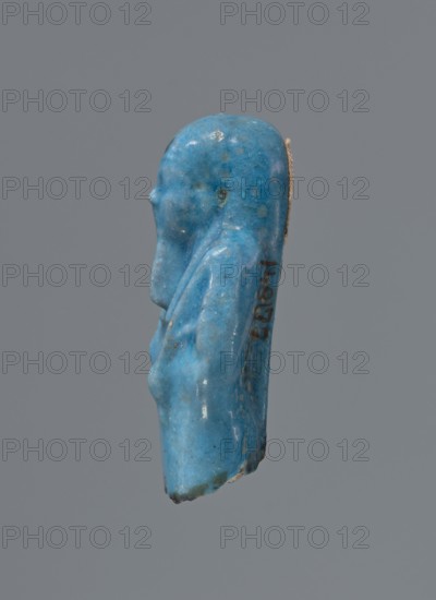 Shabti, Mummy-shaped figurine functioning as a funerary offering; mummy-shaped, supported on a pillar at the back. Legs missing. Arms crossed on the chest, right folded over left. In the right hand is a hoe, in the left a pickaxe. On the back is a bag slung on a string over the left shoulder. Convex tools. On the head is a long, smooth, tripartite wig. Long, straight beard braided. Not inscribed. 664–332 BC, Late Period, Egypt. Height 5.2 cm., A small carved blue figurine shown in profile against a gray background, with a rounded head, subtle facial features, an elongated body with a draped form, smooth glossy surface with lighter and darker blue mottling and a few small pale spots, and a thin tan cord or strip attached along the back.