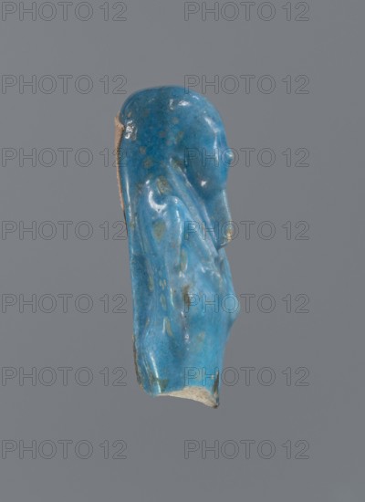 Shabti, Mummy-shaped figurine, funerary offering. Supported on a pillar at the back. Legs missing. Arms crossed on the chest, right folded over left. In the right hand is a hoe, in the left a pickaxe. On the back is a bag slung on a string over the left shoulder. Convex tools. On the head is a long, smooth, tripartite wig. Long, straight braided beard. Not inscribed. 664–332 BC; Late Period, Egypt. Shabti, height 5.2 cm., A small sculpted fragment of a human profile rendered in a glossy blue material with areas of lighter and darker blue and a few greenish spots, showing a head and upper torso with a smooth rounded head, a subtle nose, and a draped shoulder and chest, with the back edge revealing a beige, unglazed interior; the background is uniform gray.