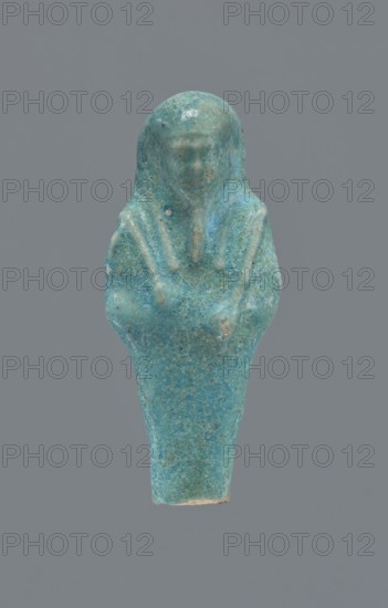 Shabti, Mummy-shaped figurine, funerary gift, supported at the back on a pillar. Legs missing from the knees down. Arms crossed on the chest, right folded over left. In the right hand is a hoe; in the left, an axe. On the back is a bag slung on a string over the left shoulder. Convex tools. On the head is a long, smooth, three-part wig. Long, straight beard braided in a plait. Facial details poorly visible. Not inscribed. 664–332 BC, Late Period, Egypt. Height: 6.6 cm., A small sculpted figure rendered in shades of turquoise and teal with areas of lighter blue and hints of green, shown against a flat gray background; the figure has a rounded head and a simplified facial area, a hood or headdress that drapes down over the shoulders, and an elongated tapered body with arms folded across the chest, the surface showing a speckled, slightly weathered texture with some tiny darker spots and lighter worn edges.