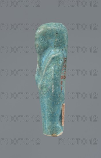 Shabti, mummy-shaped figurine supported at the back on a pillar. Legs missing from the knees down. Arms crossed on the chest, right folded over left. In the right hand is a hoe, in the left an axe. On the back is a bag slung on a string over the left shoulder. Convex tools. On the head is a long, smooth, three-part wig. Long, straight beard braided. Facial details poorly visible. Not inscribed. 664–332 BC; Late Period, Egypt. Height 6.6 cm., A small turquoise-blue carved figure with a smooth, rounded head and simplified body shape, showing a raised arm along one side and a slight suggestion of facial contour, with a few darker speckles and areas of lighter blue and green patina, a small patch of beige material attached near the lower side, and a neutral gray background.