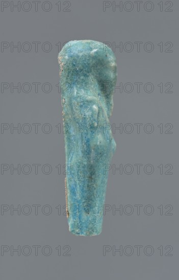 Shabti, Mummy-shaped figurine, funerary gift; supported at the back on a pillar. Legs missing from the knees down. Arms crossed on the chest, right folded over left. In the right hand is a hoe, in the left an axe. On the back is a bag slung on a string over the left shoulder. Convex tools. On the head is a long, smooth, three-part wig. Long, straight beard braided. Facial details are poorly visible. Not inscribed. 664–332 BC Late Period, Egypt. Height 6.6 cm., A small vertical figurine-like object shown in profile against a plain gray background, with a textured surface and uneven edges; the object displays shades of blue and turquoise with areas of lighter greenish-blue and small patches of pale beige on its side, and it has a rounded top, a subtle protrusion suggesting a shoulder, and a tapered lower portion.