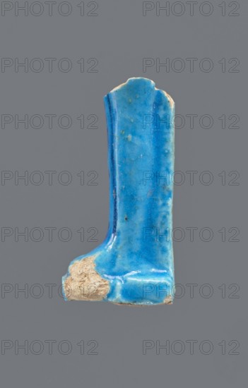 Shabti legs, Fragment of the legs of a mummy-shaped shabti figurine preserved from the knees down. The feet rest on a base, the back of the figurine supported by a pilaster. On the front of the legs is a painted hieroglyphic inscription in vertical lines. Mummy-shaped figurine, funerary gift; Late Period, Egypt, 664–332 BC. Shabti; height 8.5 cm, width 2 cm., A fragment of a glazed object with a glossy sky blue surface showing variations to deeper turquoise and small speckles, with a rough exposed beige-brown unglazed area at one end, overall L-shaped with a rounded top edge and a vertical ridge along one side, set against a plain neutral gray background.