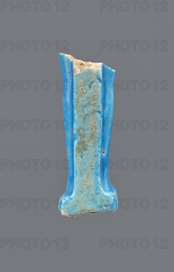 Shabti legs, Mummy-shaped figurine fragment: legs preserved from the knees down. Feet rest on a base; back supported by a pilaster. Painted hieroglyphic inscription in vertical lines on the front of the legs. Late Period, Egypt, 664–332 BC. Shabti; height 8.5 cm, width 2 cm., A vertical fragment of a glazed ceramic object shown against a solid gray background, with a glossy surface in shades of bright blue and a paler turquoise blue on the central raised area; the piece has irregular, broken edges revealing a rough, beige inner material, and the glazed surface shows small pits and areas of brownish discoloration; the shape widens slightly at the bottom with rounded protrusions and has two fluted vertical ridges along the sides.