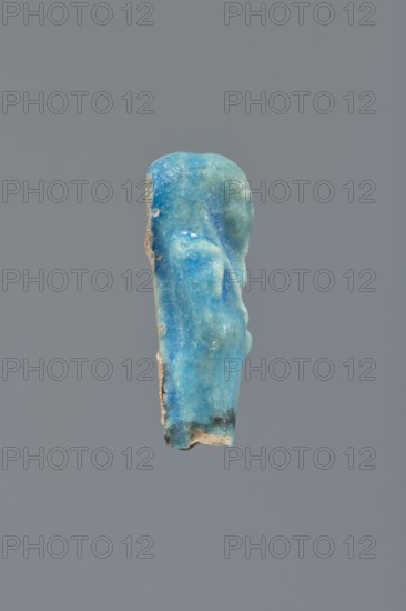 Shabti, Mummy-shaped figurine, funerary gift; supported on a pillar at the back. Legs missing. Arms crossed on the chest, right folded over left. In the right hand, a hoe; in the left, a pickaxe. On the back, a bag slung on a string over the left shoulder. Convex tools. On the head, a long, smooth, three-part wig. Long, straight beard braided. Facial details poorly visible. Not inscribed. 664–332 BC, Late Period, Egypt. Height 5.4 cm., A small, worn vertical object with an irregular rounded top and uneven surface in shades of bright blue, turquoise, and teal, with areas of lighter aqua and pale blue, and a few darker blue spots; the edges show rough beige and tan material with small patches of dark gray or black near the bottom; it is set against a flat medium-gray background.