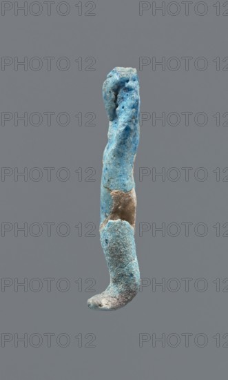 Shabti, Mummy-shaped figurine, funerary gift. Legs missing. Arms crossed on the chest; hands invisible from under the shroud. Smooth, tripartite wig on the head. Facial details invisible. Not inscribed. 664–332 BC Late Period, Egypt. Height 3.7 cm., A single elongated irregular object suspended against a plain gray background, with a rough textured surface showing a mix of blue and turquoise tones, areas of muted brownish-beige, and small spots of darker blue; the object tapers and curves slightly at one end and has pitted, uneven contours with visible granular and weathered surfaces.