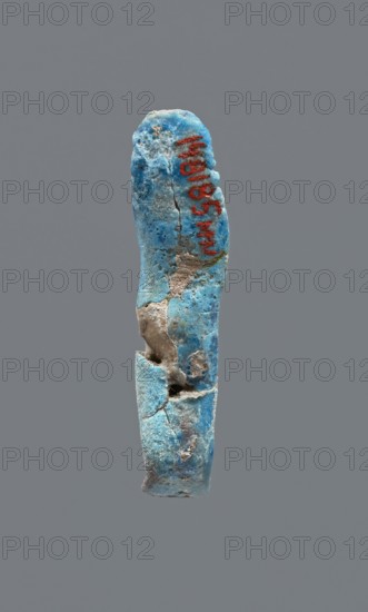 Shabti, mummy-shaped figurine, funerary gift. Legs missing. Arms crossed on the chest. Hands invisible from under the shroud. Smooth tripartite wig on the head. Facial details invisible. Not inscribed. Late Period, 664–332 BC, Egypt. Height 3.7 cm., A broken elongated object with a rough, pitted surface suspended against a plain gray background, showing a predominantly blue coloration with areas of pale blue and turquoise, patches of beige and tan where material is missing, and small dark gray spots; the object has visible cracks and holes, an irregular rounded top and a fractured lower section, and a streak of a bright red color on one side.