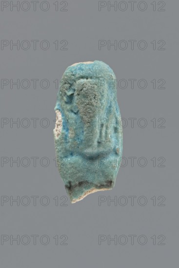 Shabti, Mummy-shaped funerary figurine, legs missing. Arms crossed on the chest, hands invisible under the shroud. Long, smooth, three-part wig; wide, straight, smooth beard. Not inscribed. Late Period, Egypt, 664–332 BC. Height 3.8 cm., A small roughly cylindrical object with an uneven, weathered surface in shades of blue and turquoise with areas of pale off-white and a few darker bluish-gray spots; the object has irregular edges and a rough, granular texture with a concave impression on one side and subtle raised ridges suggesting a simplified outline, all shown against a plain medium-gray background.