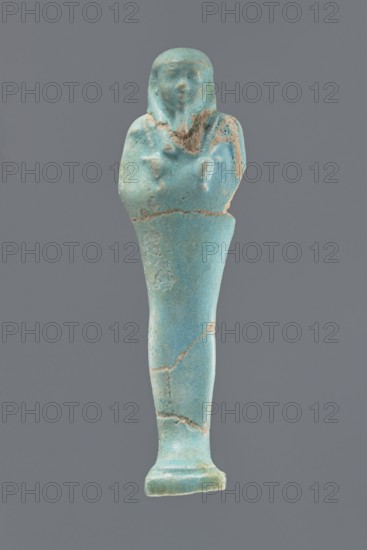 Ushabti, Mummy-shaped figurine, standing on a base with a narrow, slightly convex pillar at the back. Arms crossed high on the chest, right folded over left. Left hand holds a pickaxe, right a mattock, with a twisted rope passed over the left shoulder; a bag is on the back at the end of the rope. Wears a smooth, three-part wig and a long straight beard. Facial details poorly legible. Not inscribed. Ptolemaic Period, 332–30 BC; Egypt. Height 12.1 cm., A single elongated statuette in shades of turquoise and light blue with areas of pale tan where the surface is worn, showing a humanlike figure with a rounded head and simplified facial features, a suggestion of hair or head covering, crossed arms over the chest, a narrow tapering lower body, and a small flared base, all set against a solid medium gray background.